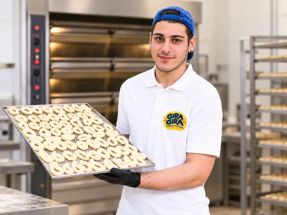 Un fornaio Gira Gira con una teglia di taralli appena formati, davanti al forno